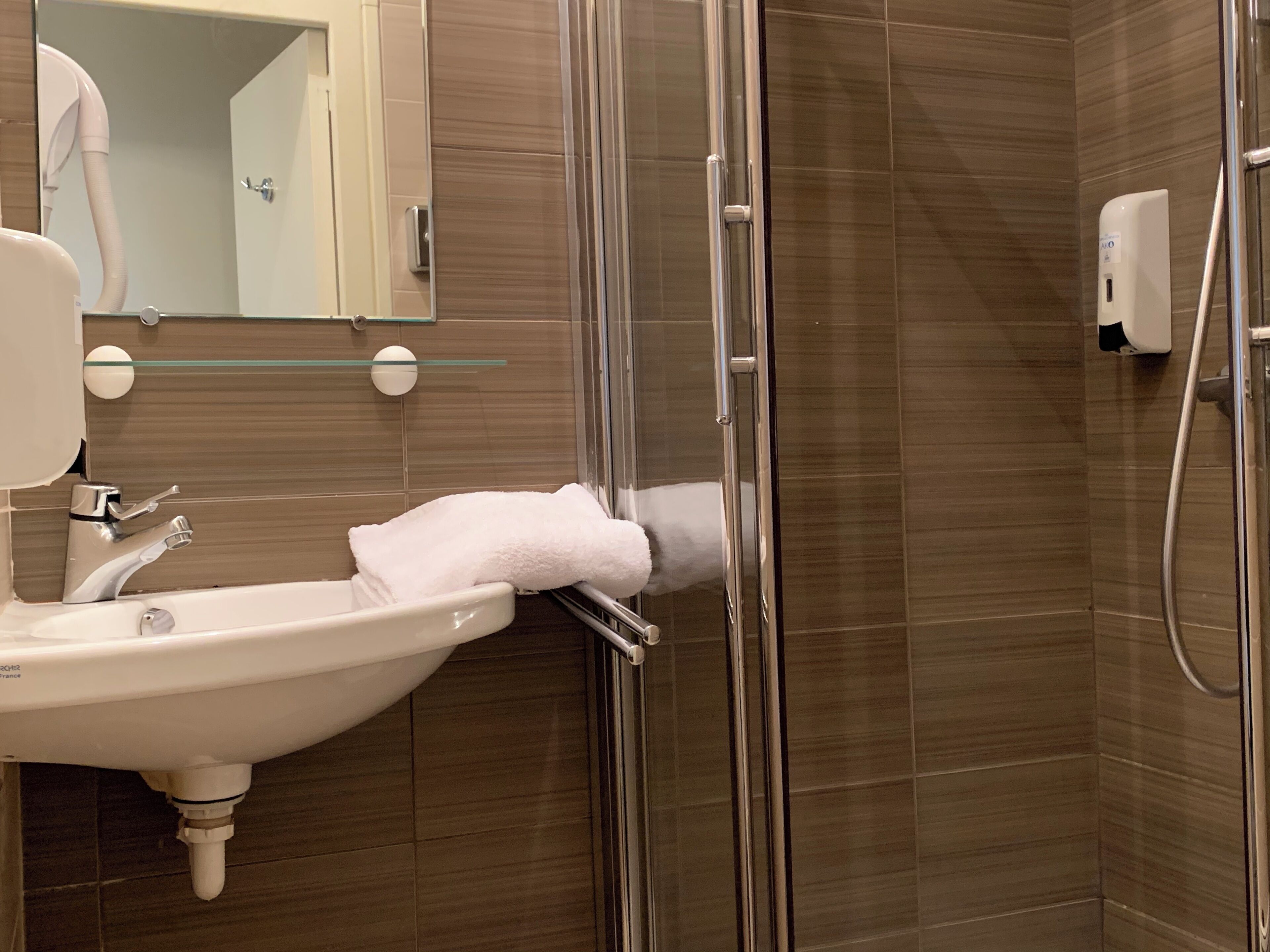 A modern bathroom with a glass shower enclosure, a white sink, and a hand dryer.