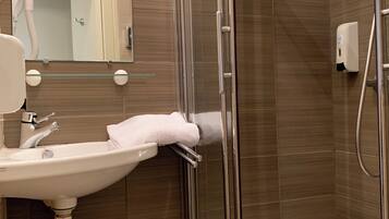 A modern bathroom with a glass shower enclosure, a white sink, and a hand dryer.