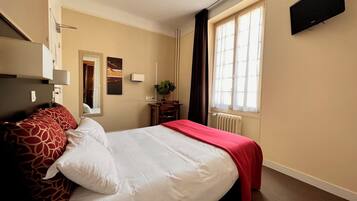 Une chambre d’hôtel avec un lit, un bureau, une chaise, une plante et une fenêtre.