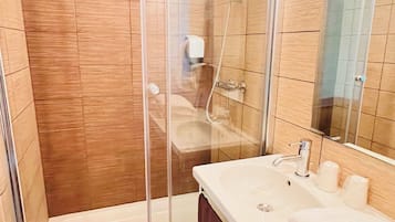 Un baño moderno con ducha de vidrio, lavamanos blanco y un espejo grande.