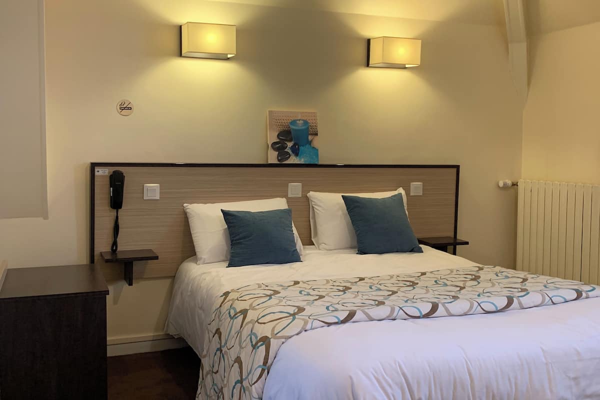 A hotel room with a bed, two bedside lamps, a telephone, and a decorative item on the headboard.