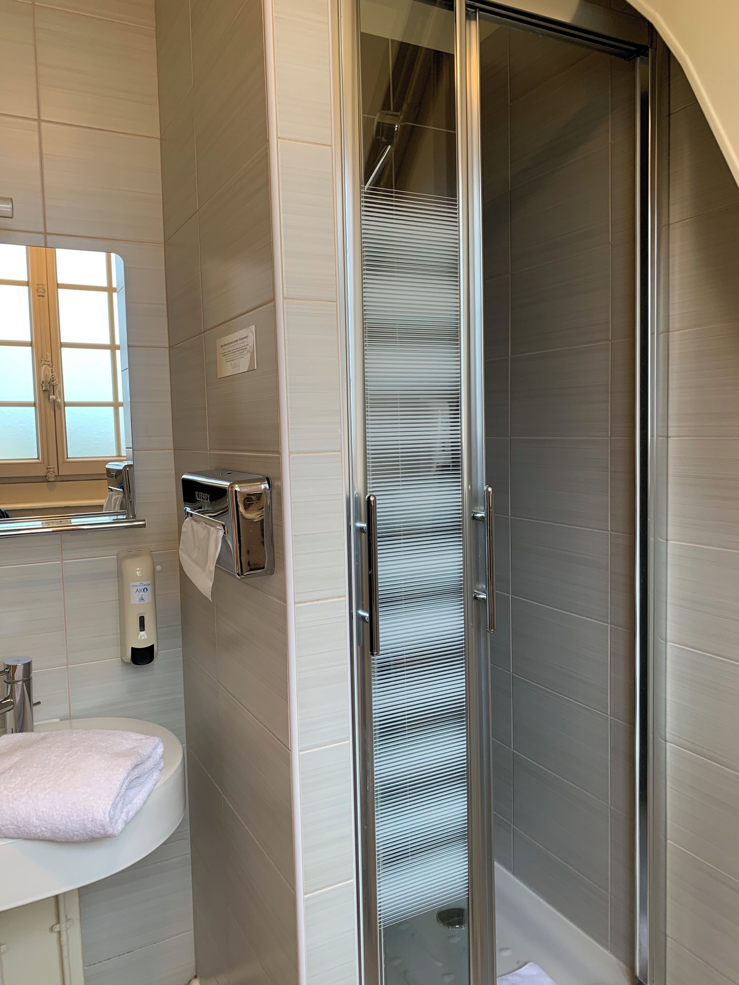 A modern bathroom with a glass-enclosed shower, a sink with a towel, and a hand dryer.