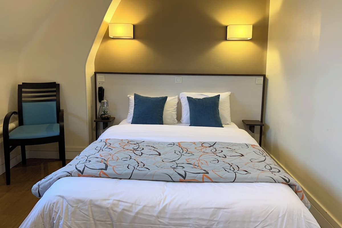 A hotel room with a bed, two bedside lamps, a chair, a bedside table with a lamp, and a phone.