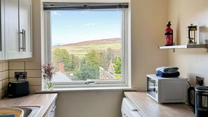 A kitchen with a view of a green landscape, a red fire extinguisher, and a white microwave. - 2 bedroom accommodation in Wooler (Wooler)