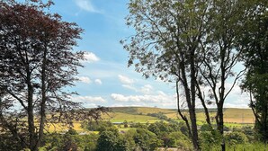 A rural landscape with a fence, trees, and a distant view of a village. - 2 bedroom accommodation in Wooler (Wooler)
