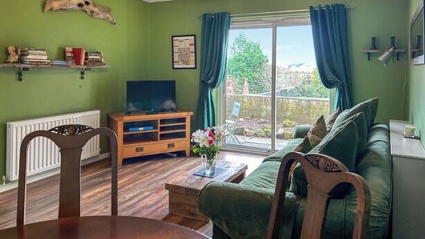 A living room with a green wall, wooden furniture, a television, and a view of the outdoors. - 2 bedroom accommodation in Wooler (Wooler)