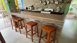 A kitchen with a granite countertop, a gas stove, a microwave, and a sink. There are three wooden stools and a green wall with a decorative sticker.