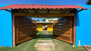 A wooden gate leading to a building with a red roof and blue walls.