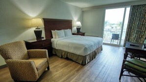 A hotel room with a large bed, a chair, a desk, and a balcony with a view. - King Standard Room Pool Side (Treasure Island)
