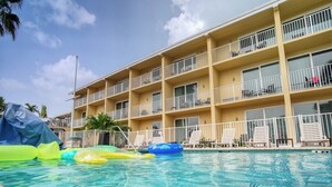 Une piscine avec des jeux gonflables, un immeuble d’hôtel à plusieurs étages doté de balcons, et un ciel dégagé.