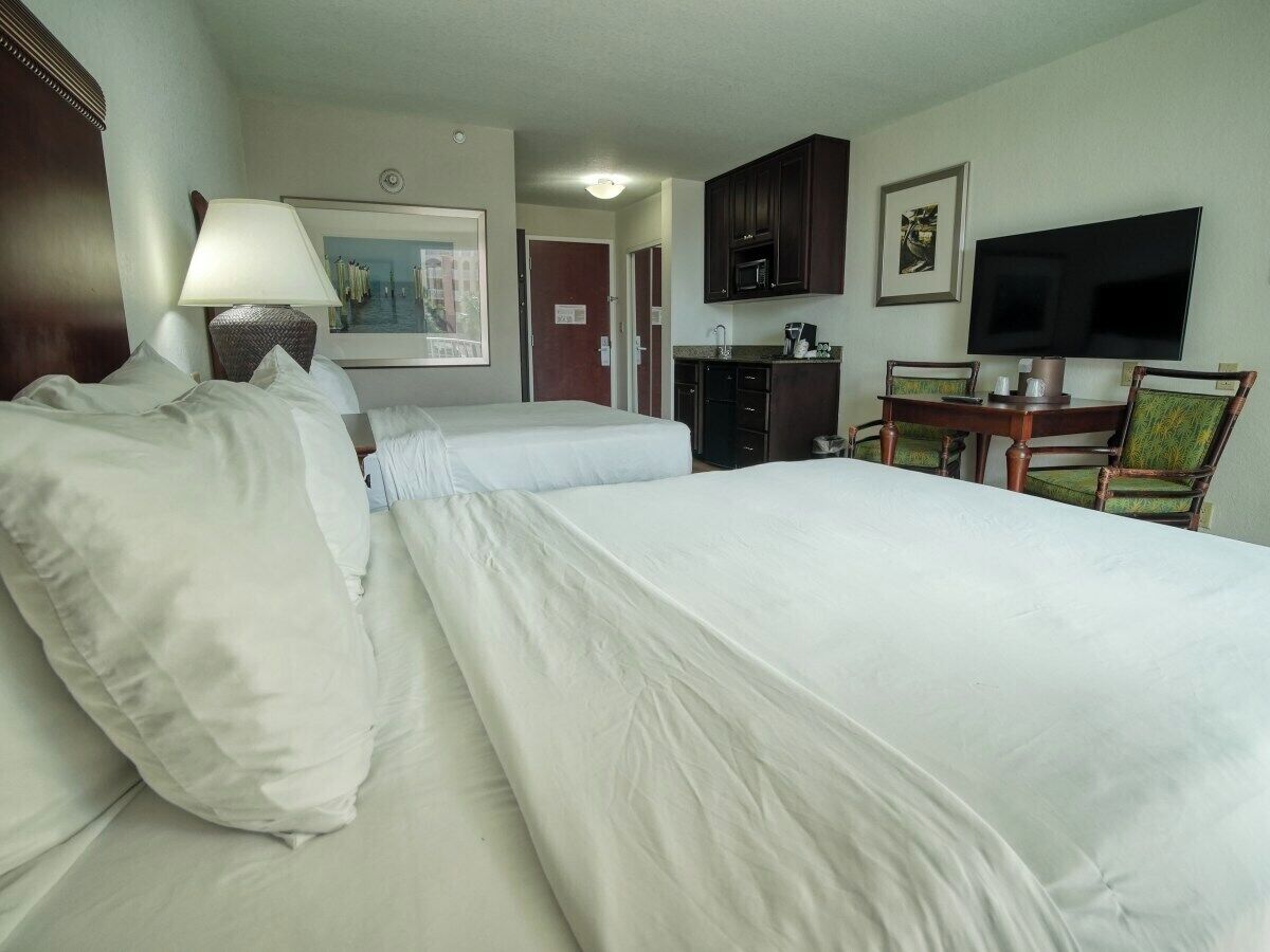 A hotel room with two beds, a desk with a chair, a television, and a small kitchenette.