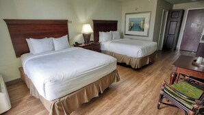 Hotellihuone, jossa on kaksi sänkyä, puulattia, tuoli ja työpöytä, jossa on lamppu.