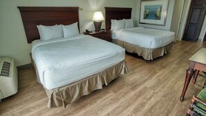 A hotel room with two beds, wooden headboards, a bedside table with a lamp, a heater, and a framed picture on the wall. - Queen Queen Poolside (Treasure Island)