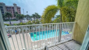 A balcony with a view of a swimming pool, palm trees, and a distant building. - Queen Queen Poolside (Treasure Island)