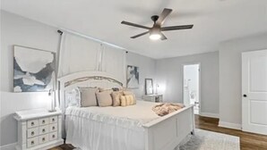 Ein Schlafzimmer mit einem Bett, Nachttischen, einem Deckenventilator und Kunstwerken an den Wänden.