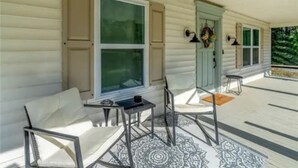 Eine überdachte Veranda mit zwei weißen Stühlen, einem kleinen Tisch und einem dekorativen Teppich.