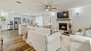 Ein geräumiges Wohnzimmer mit Kamin, weißen Sofas und einer Küche im Hintergrund.