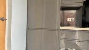 Une cuisine avec un réfrigérateur en acier inoxydable, une porte en bois et un sol carrelé.