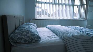 A bedroom with a bed, a window with blinds, and a radiator.