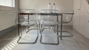 Une cuisine moderne avec une table et des chaises en verre, des meubles blancs et une fenêtre avec des stores.