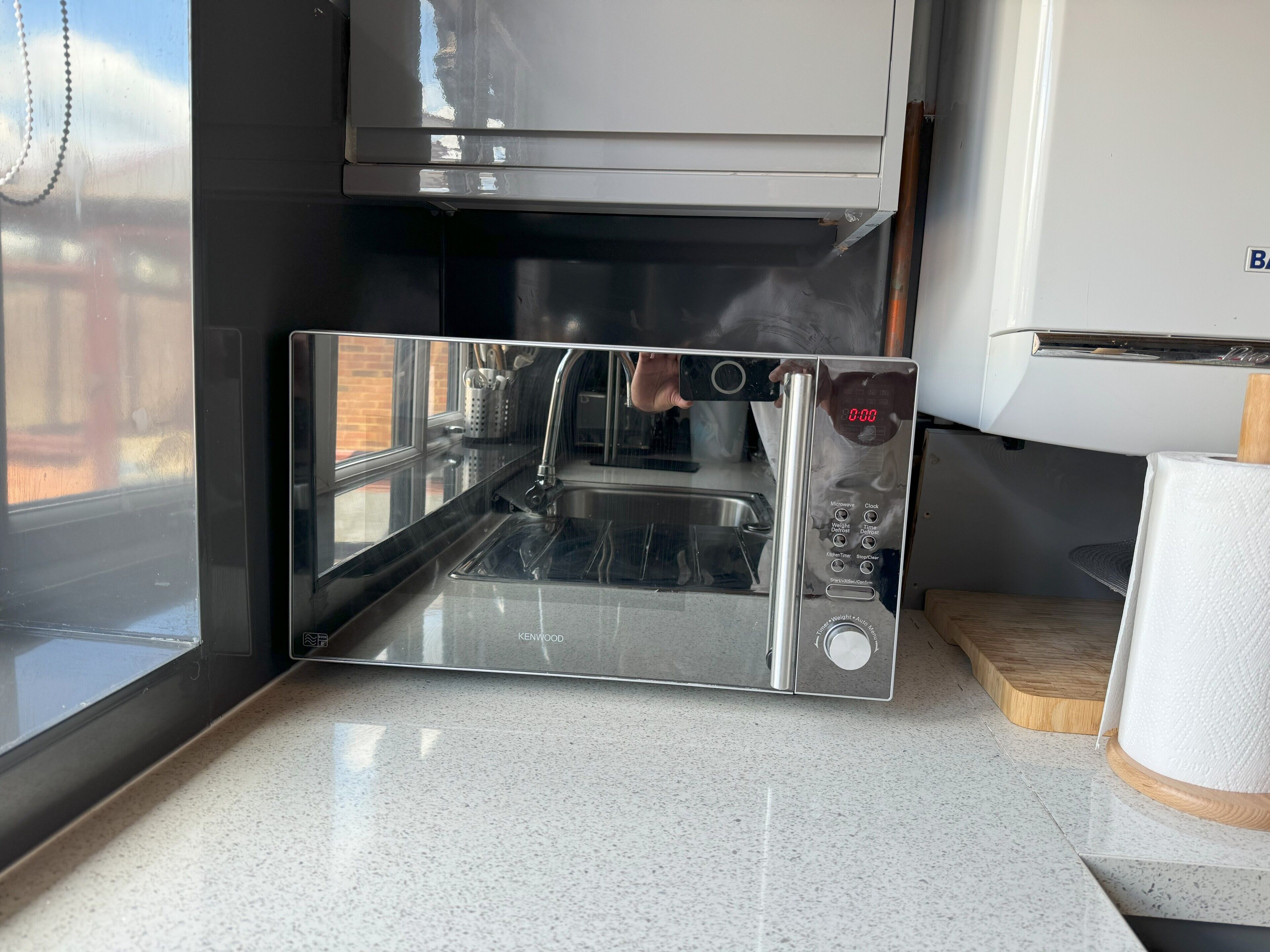 A modern kitchen with a stainless steel sink, a microwave, and a Kenwood brand coffee maker.