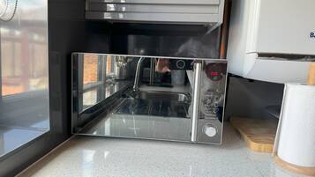 A modern kitchen with a stainless steel sink, a microwave, and a Kenwood brand coffee maker.