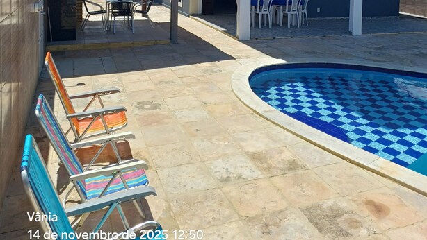 Una casa de dos pisos con piscina, mobiliario exterior y un patio cubierto.