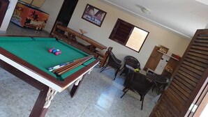 Una mesa de billar con bolas, un banco de madera, sillas de mimbre y un cuadro en la pared.