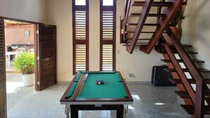 Una mesa de billar en una habitación con una escalera y ventanas amplias.