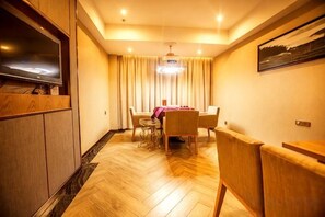 Une chambre d’hôtel avec un plancher en bois, un coin repas avec une table et des chaises, un téléviseur posé sur un meuble en bois et un tableau accroché au mur.