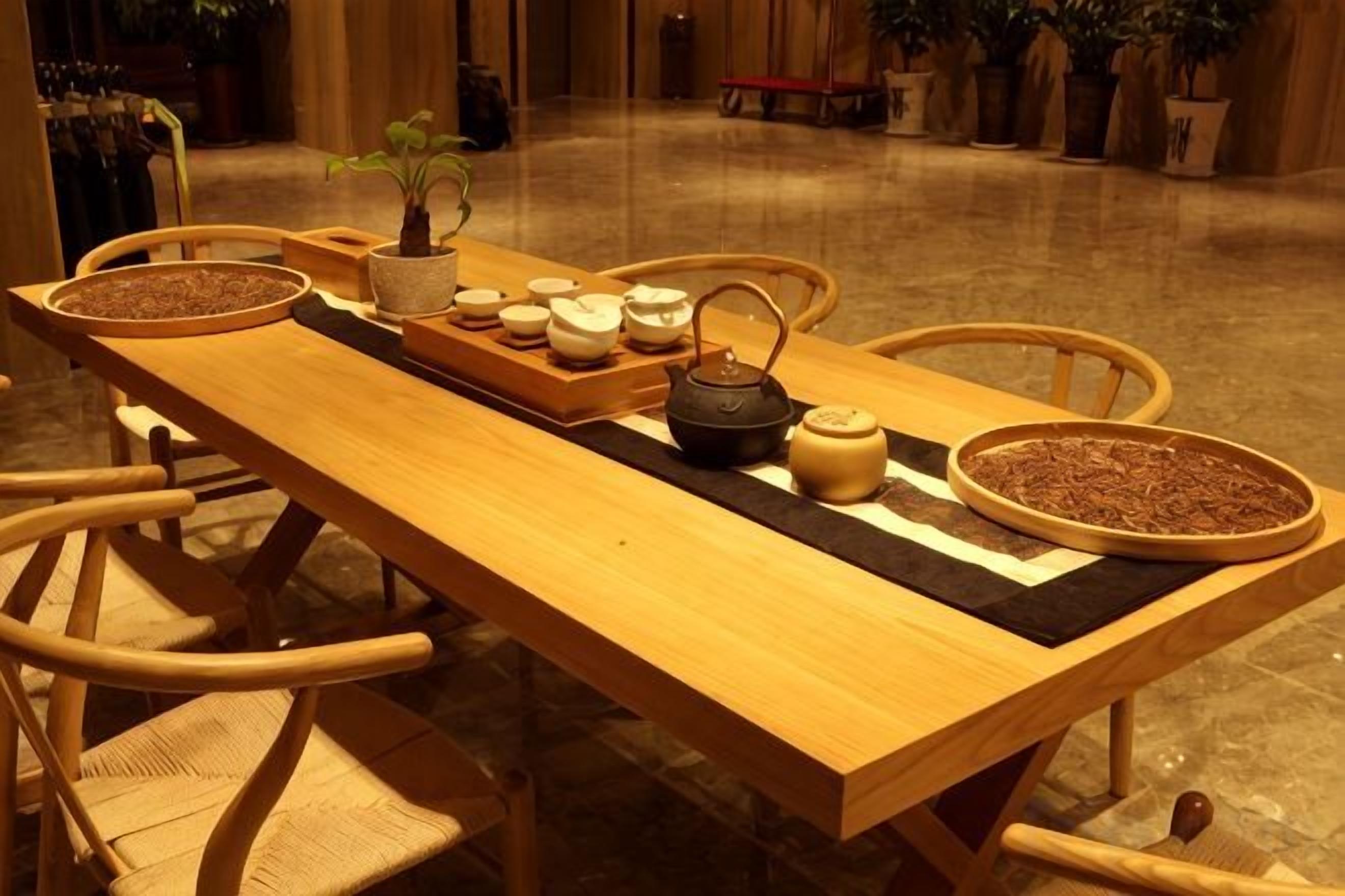 A wooden table with a tray of tea utensils, a teapot, and a bowl of tea leaves.