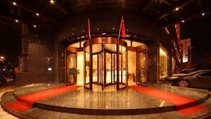 A revolving door entrance with a red carpet, a glass door, and two flags. - Soaring Dragon Tea Culture Hotel (Hanzhong High-speed Railway Station Wanbang Flagship) (Hanzhong)