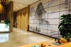Un área de recepción con un mostrador de madera, una pared grande con un cuadro tradicional y una planta en maceta.