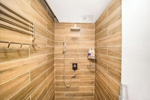Ducha con azulejos de madera, cabezal de ducha de mano y panel de control en la pared.
