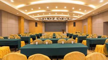 A conference room with multiple tables and chairs, a stage with a screen, and a podium.