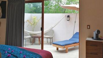 A bedroom with a bed, a desk, a chair, and a hammock outside the sliding glass door.
