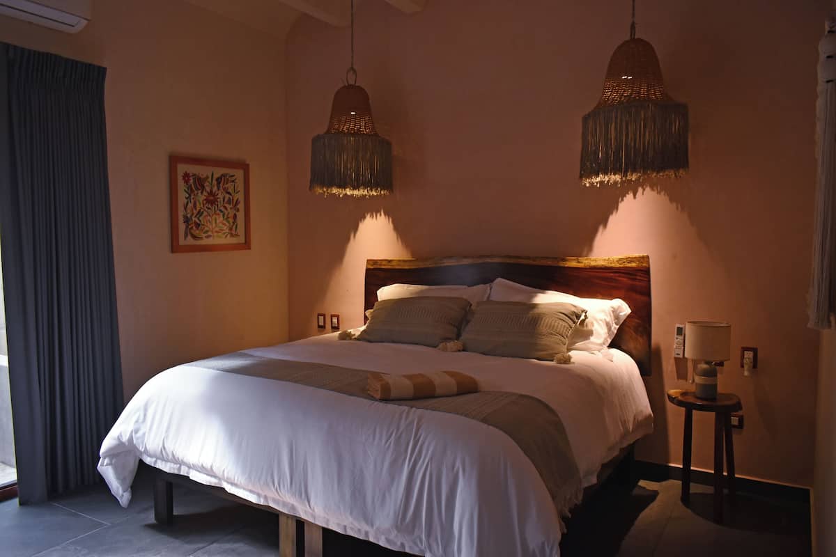 Un lit bien fait, avec une tête de lit en bois, deux lampes suspendues et une petite table de chevet avec une lampe.
