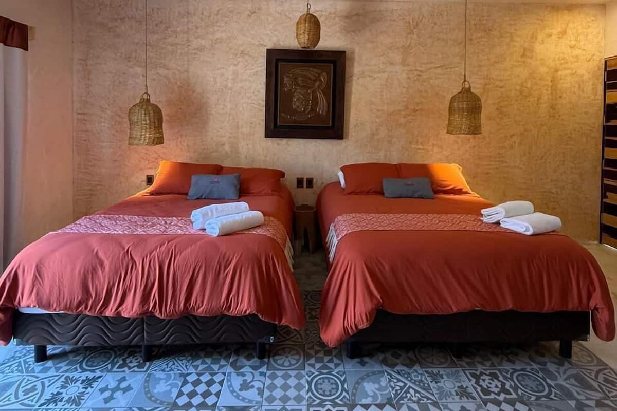 Une chambre d’hôtel avec deux lits, un ventilateur de plafond, des carreaux de sol à motifs et un tableau encadré au mur.