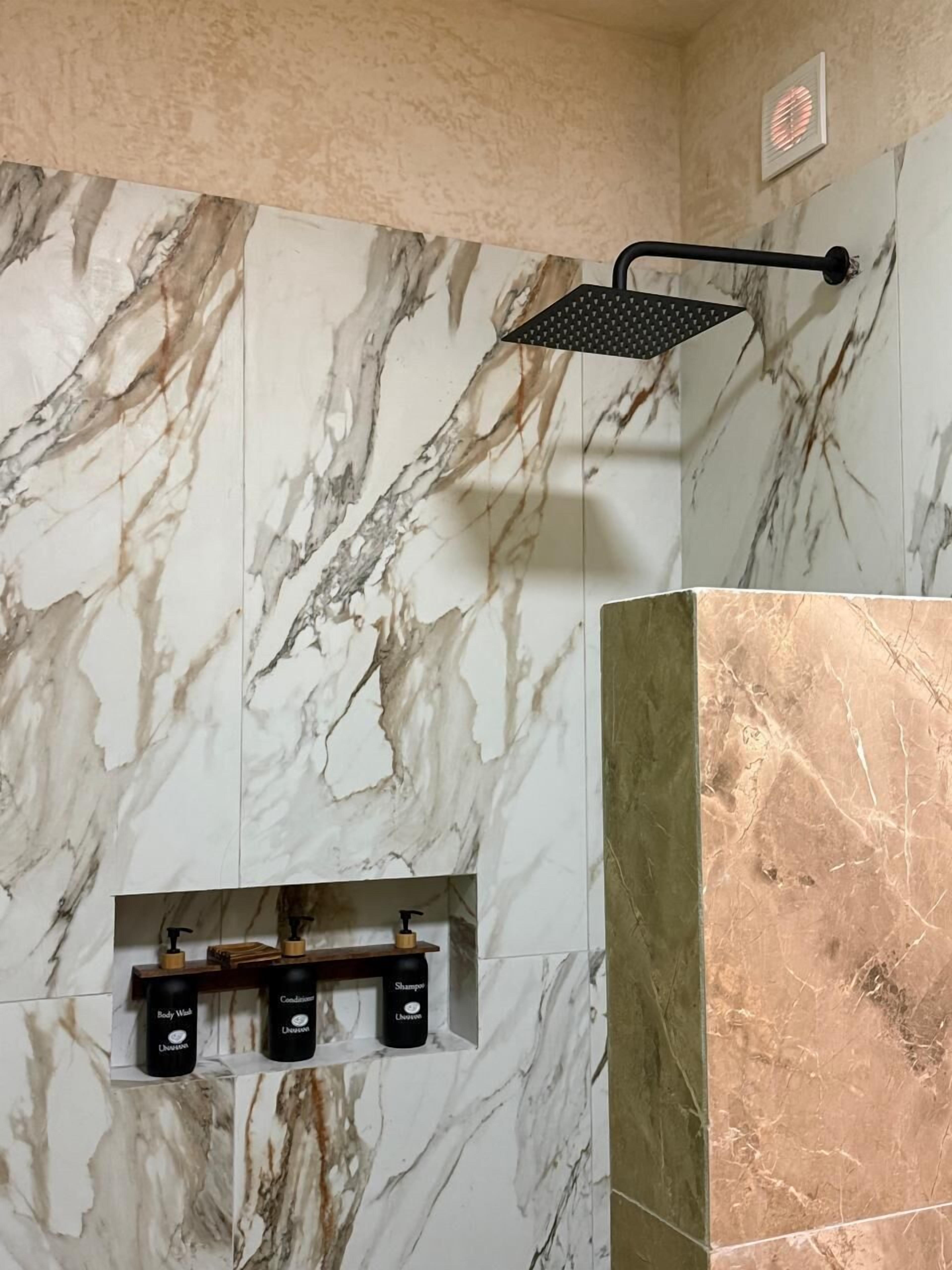 A bathroom with marble walls, a showerhead, and toiletries.