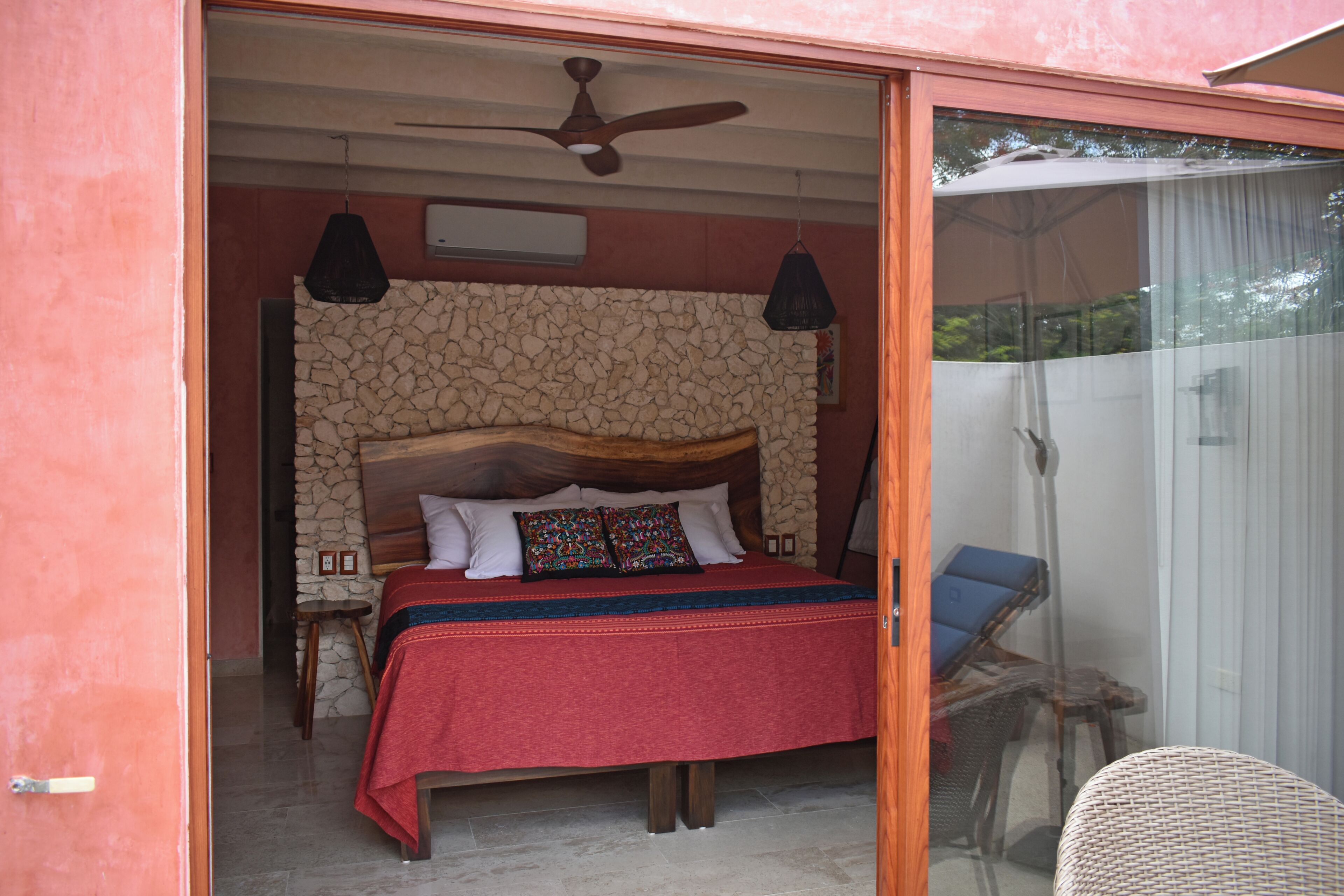 A bedroom with a stone wall, a wooden bed frame, and a ceiling fan.