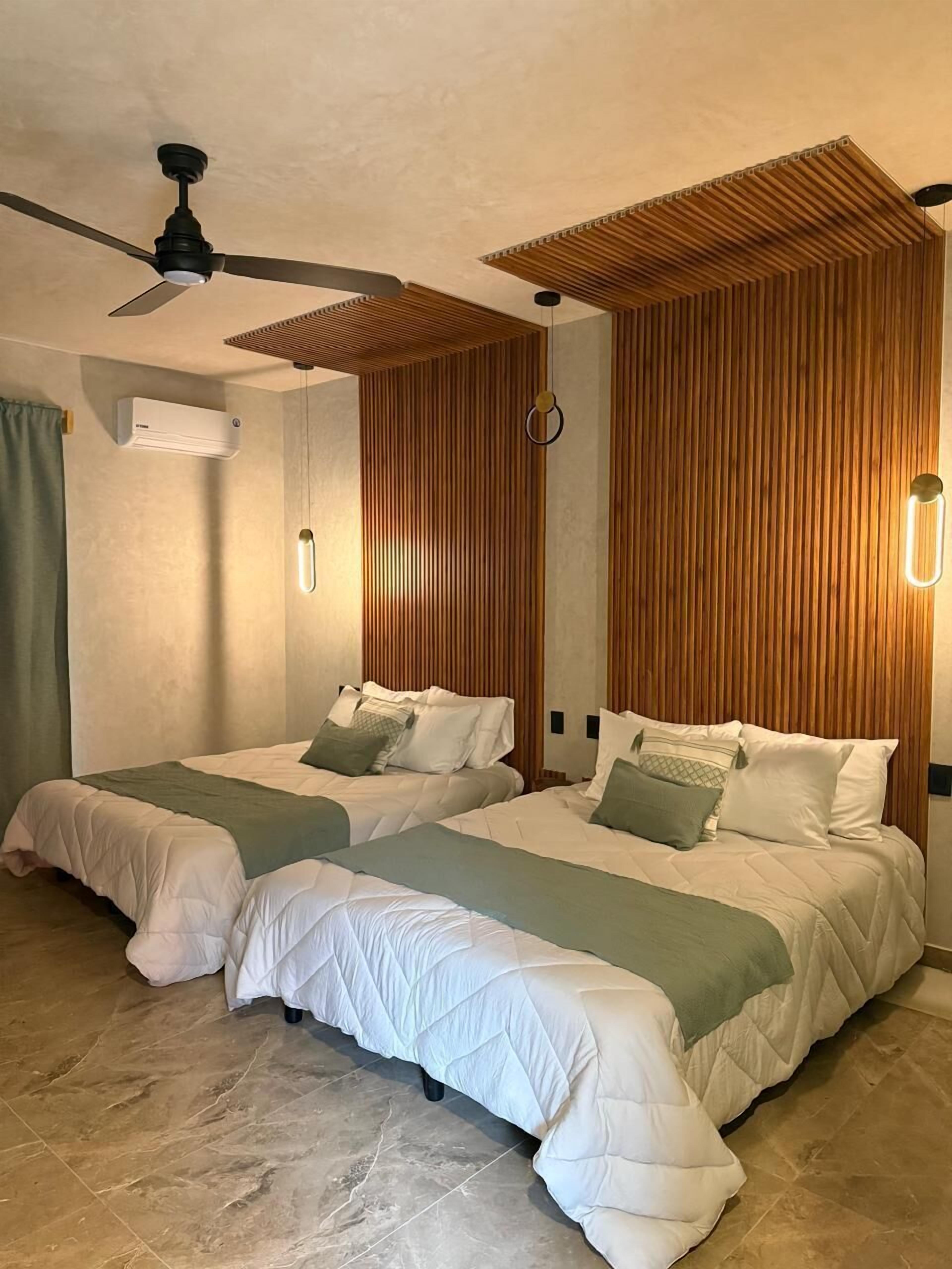 A hotel room with two beds, a ceiling fan, wooden paneling, a wall-mounted air conditioner, and a marble floor.