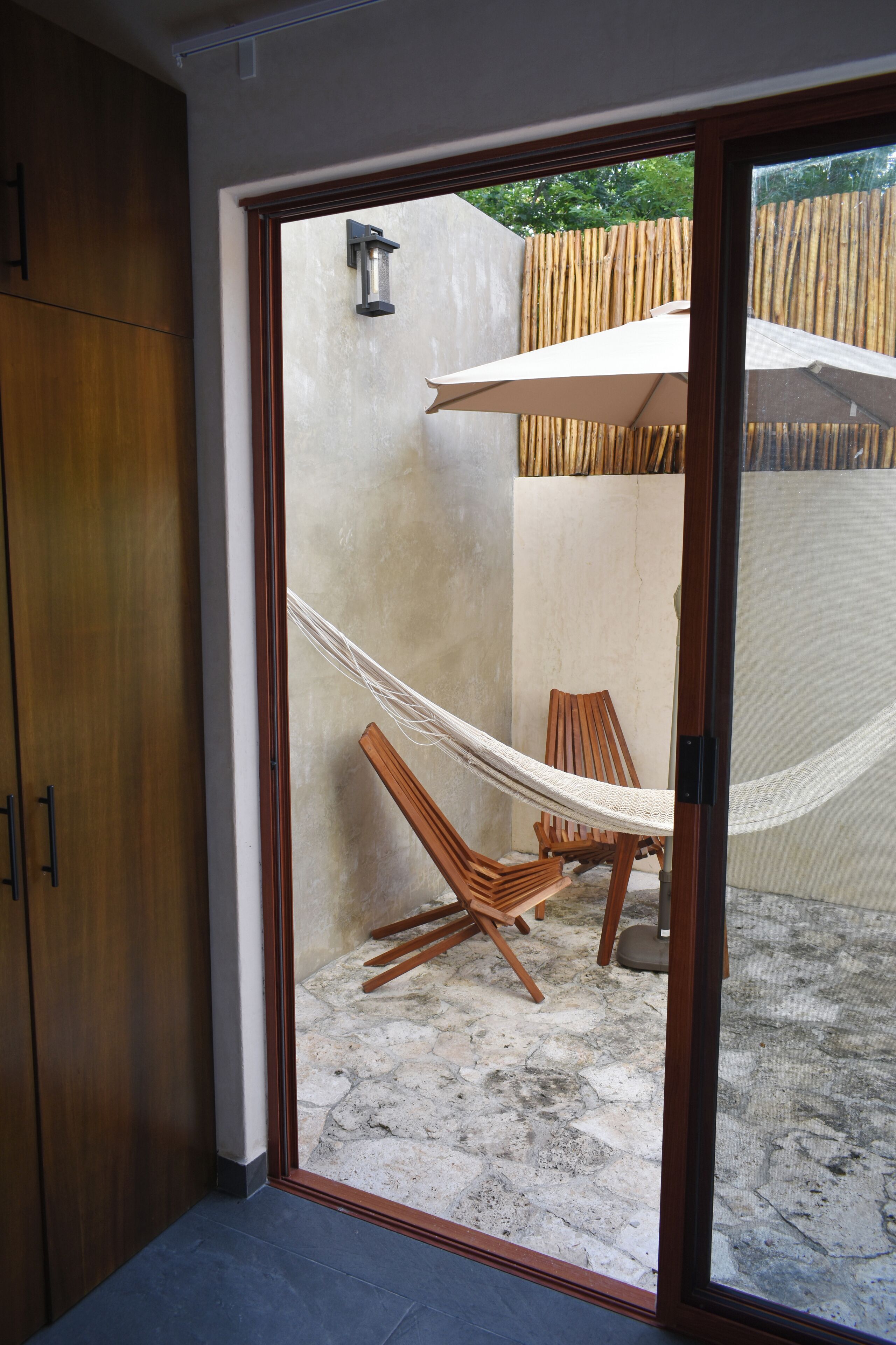 A room with a wooden door, a hammock, a wooden chair, and a large umbrella.