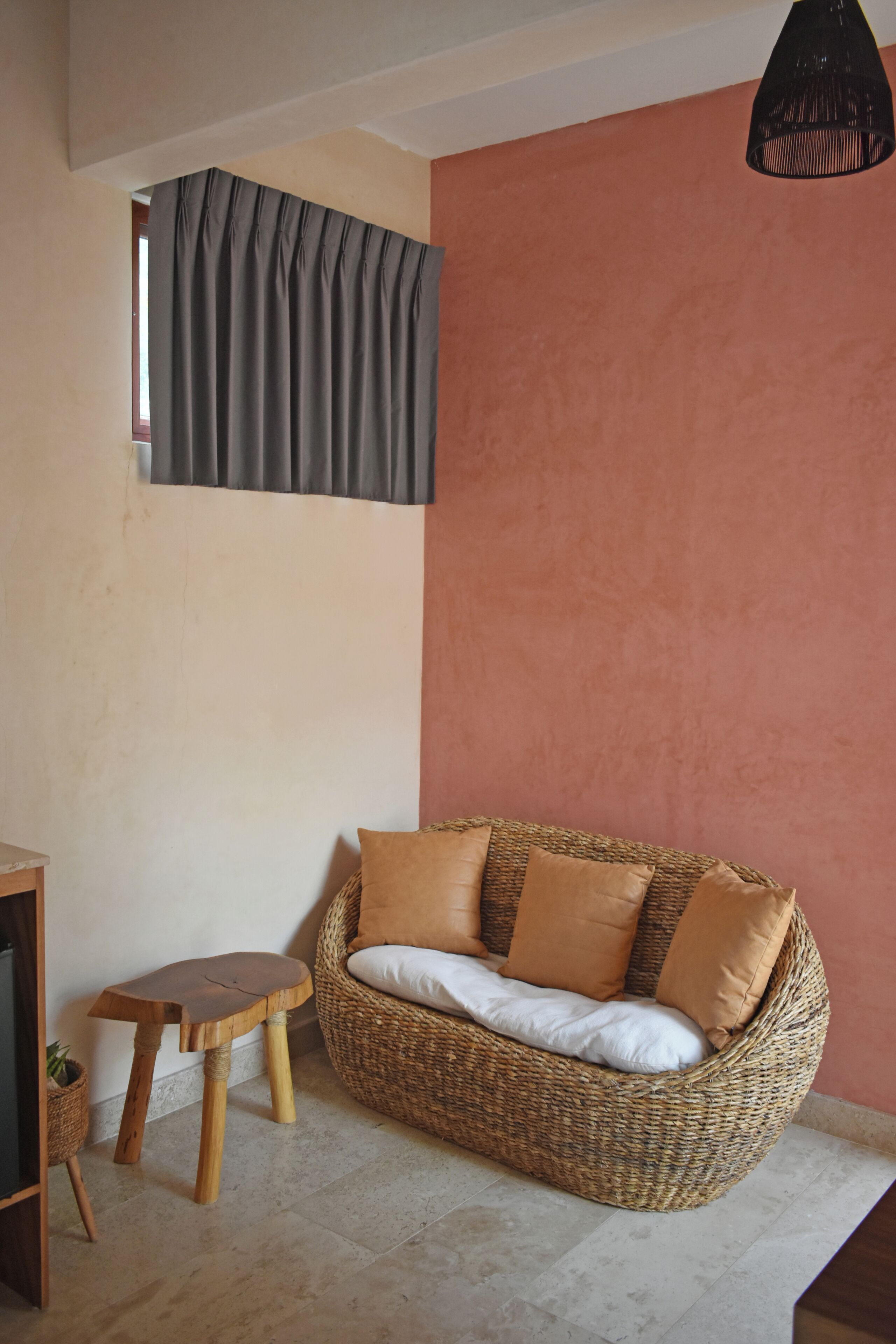 A room with a woven sofa, a small wooden stool, and a window with curtains.