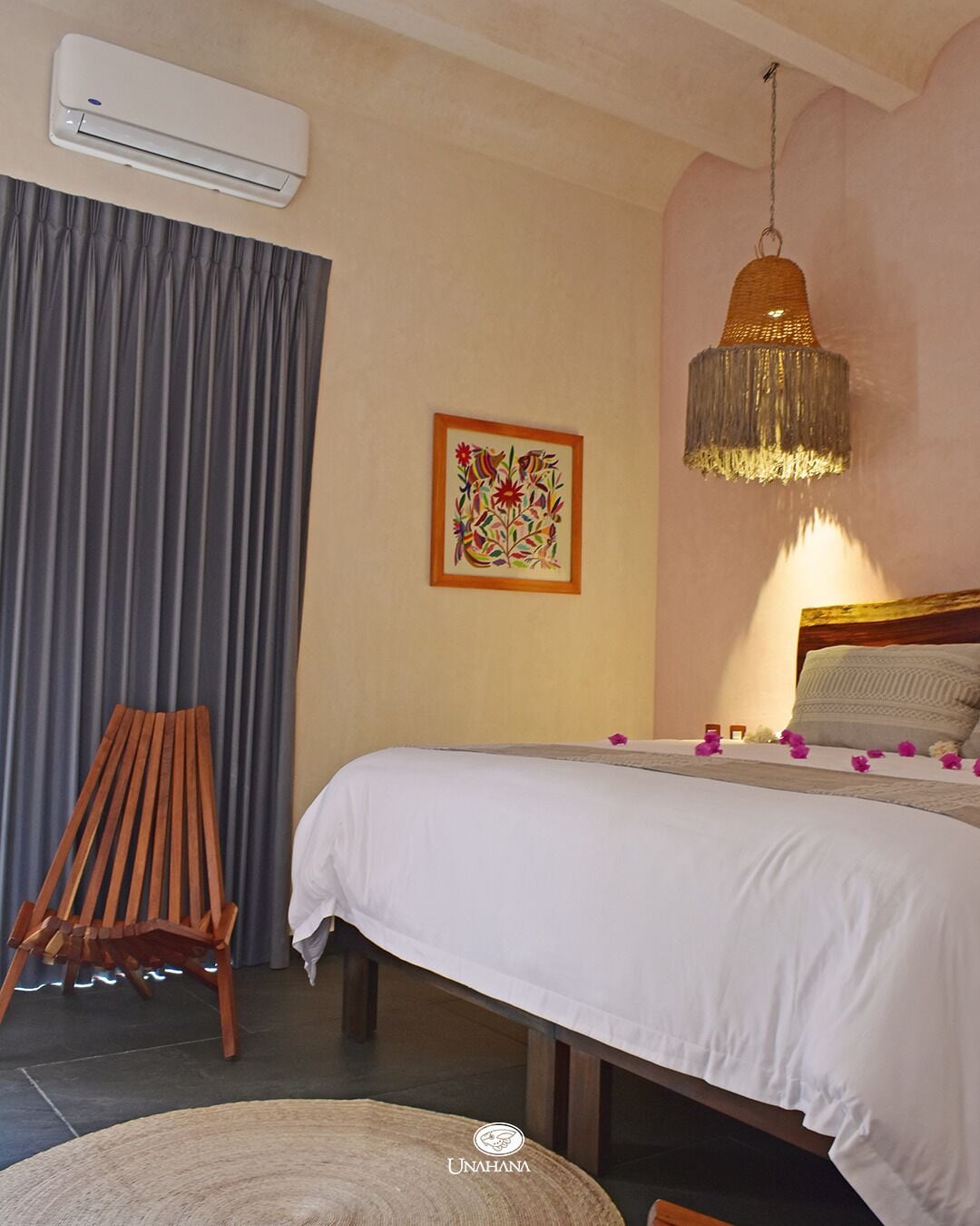 A bedroom with a bed, an air conditioner, a wooden chair, a rug, and a hanging light fixture.