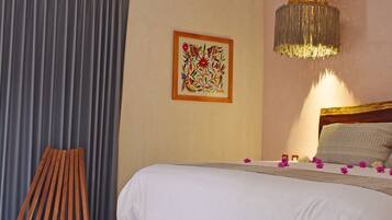 A bedroom with a bed, an air conditioner, a wooden chair, a rug, and a hanging light fixture.