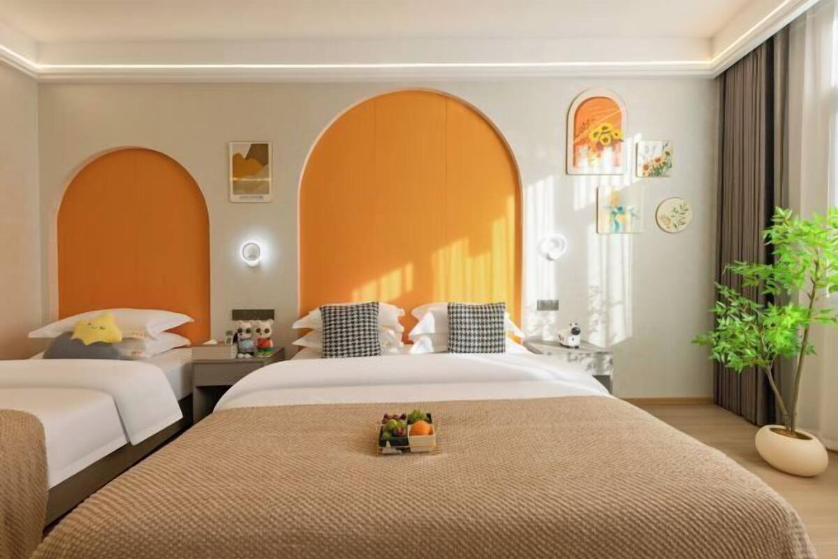 A hotel room with two beds, a large mirror, a potted plant, and a fruit basket on the bed.