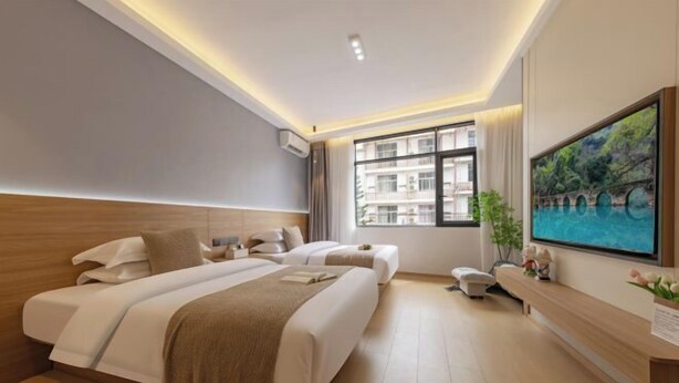 Una habitación de hotel moderna con dos camas, un ventanal con vistas a la ciudad, un televisor de pantalla plana y un pequeño rincón de descanso.