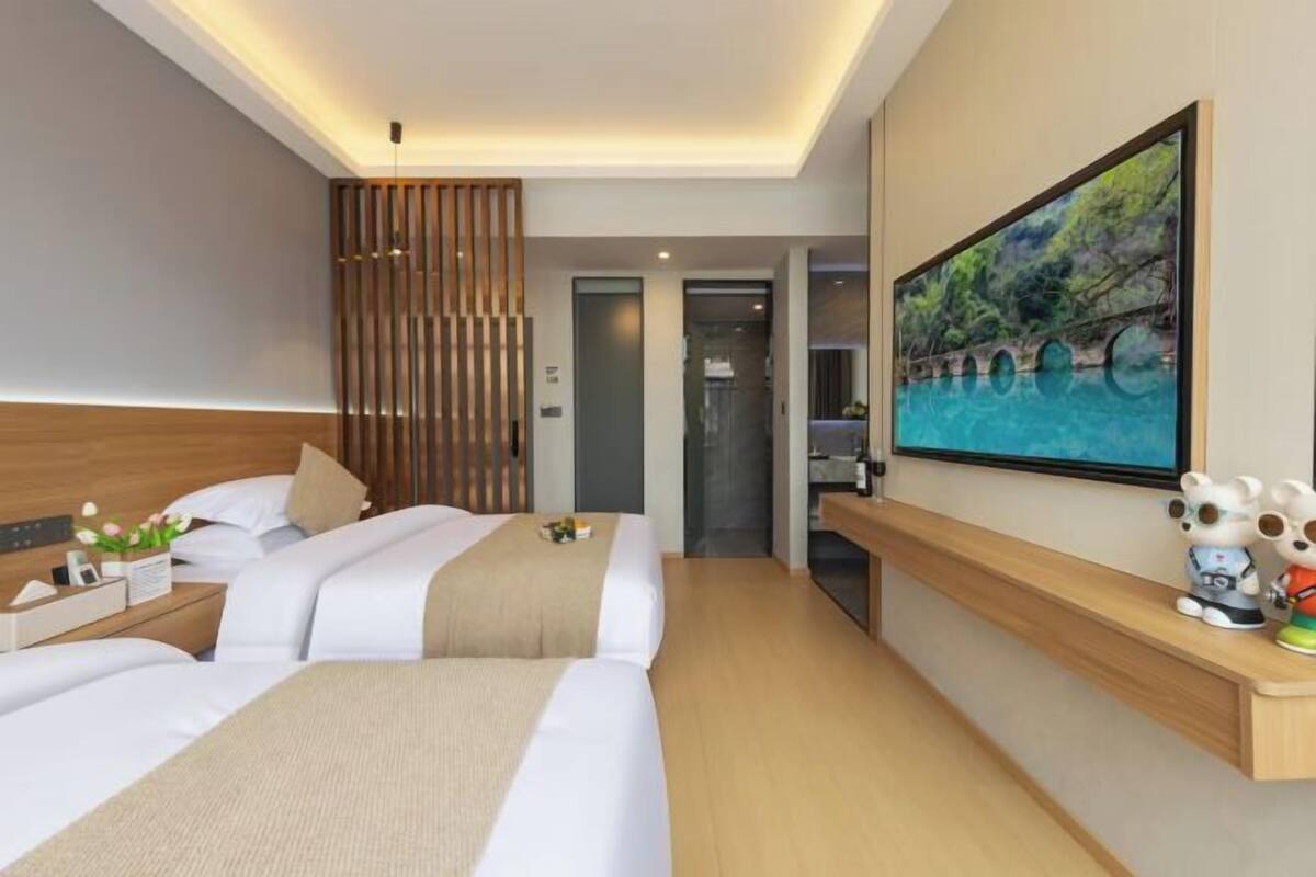 A modern hotel room with two beds, a wooden headboard, a large painting, and a small shelf with figurines.