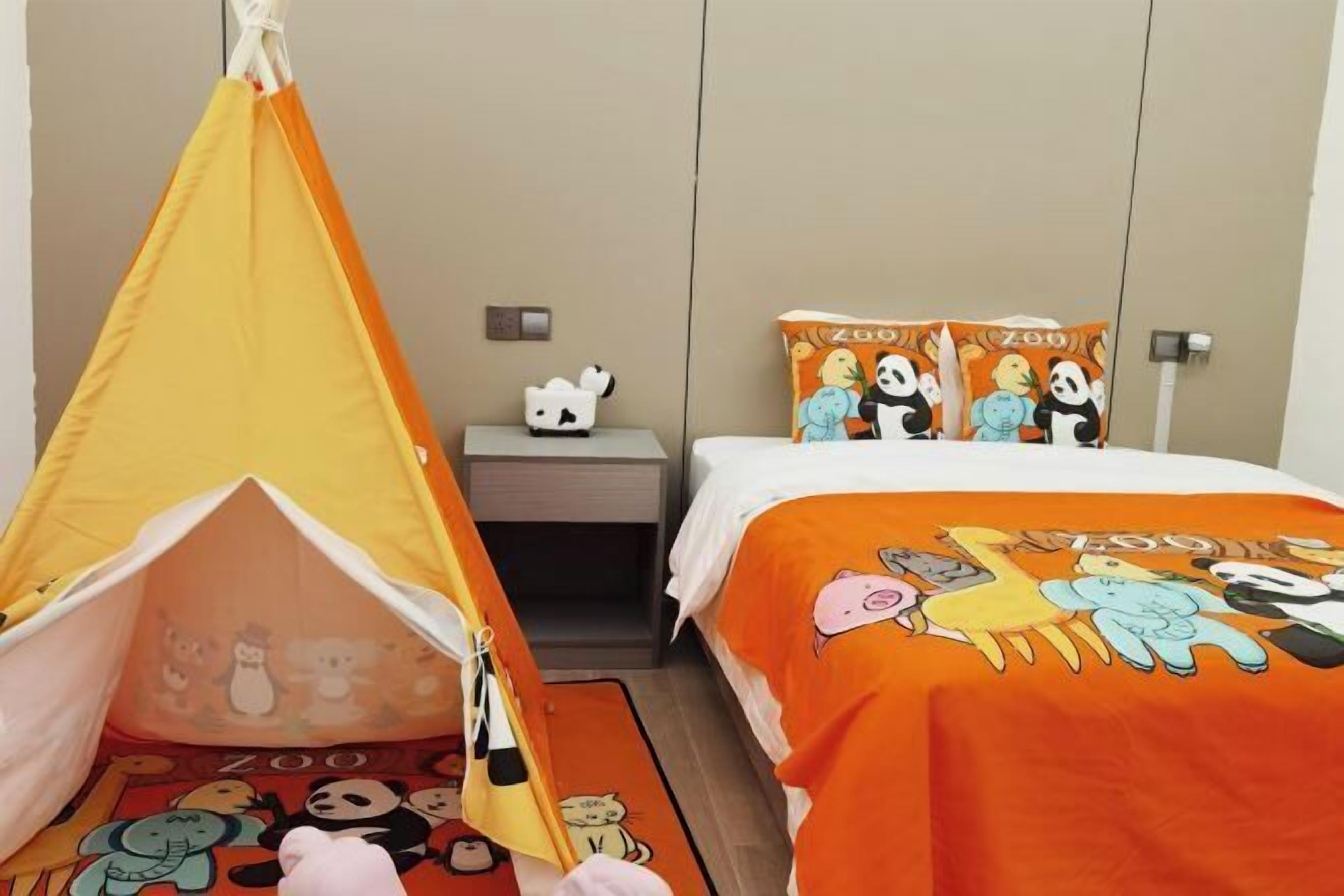 A hotel room with a bed, a small table, a chair, and a tent-like structure with cartoon characters.