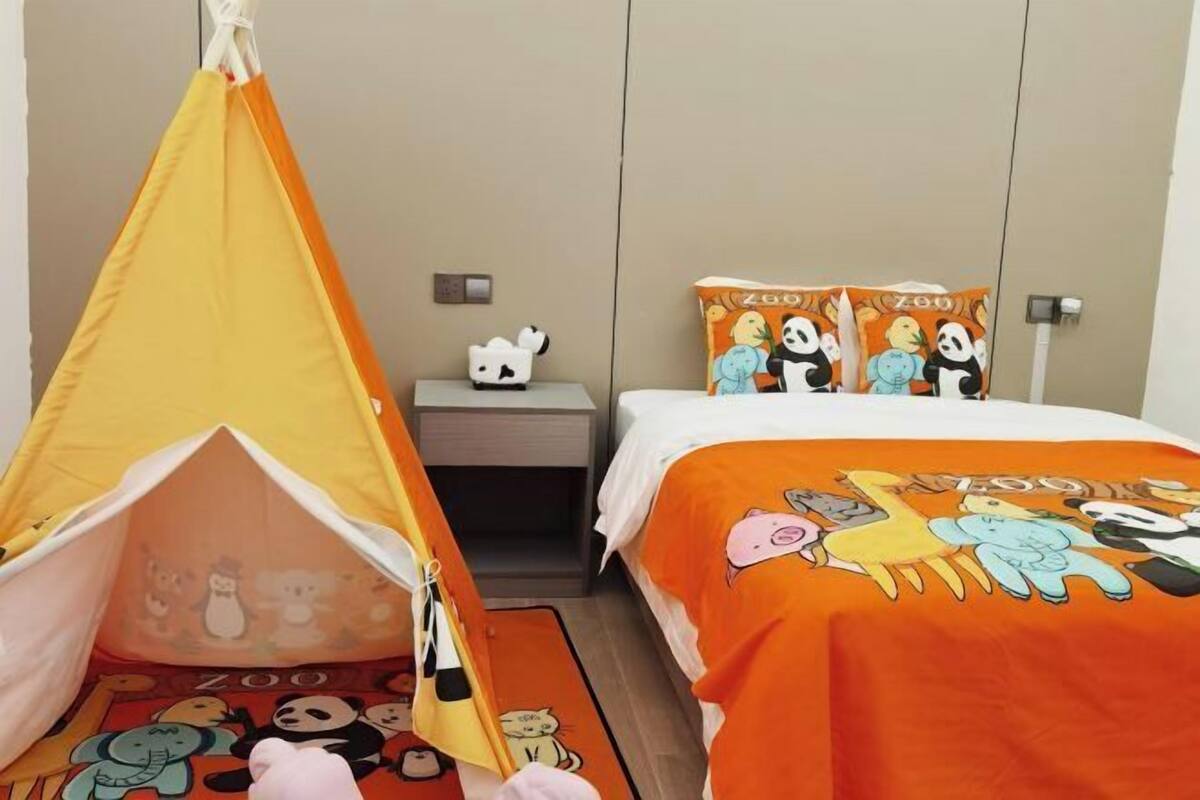 A hotel room with a bed, a small table, a chair, and a tent-like structure with cartoon characters.